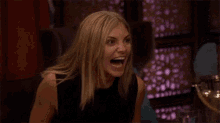 a woman in a black dress is sitting at a table with her mouth open .