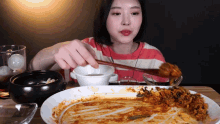 a woman in a red and white striped shirt is eating a plate of food with chopsticks