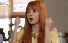 a woman with red hair is wearing a yellow shirt and holding her fist in the air .