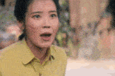 a woman in a yellow shirt is making a surprised face with her mouth open .