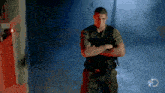 a man stands with his arms crossed in a dark room with a discovery logo in the corner