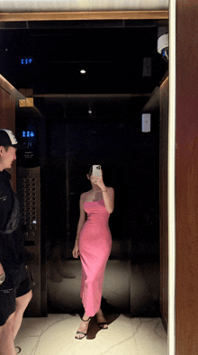 a woman in a pink dress is taking a picture of herself in a mirror