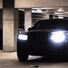 a black car is parked in a garage with its lights on .