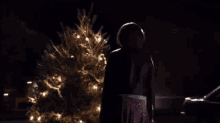a woman stands in front of a christmas tree with lights on it