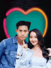 a man and a woman are posing for a picture with a neon heart in the background