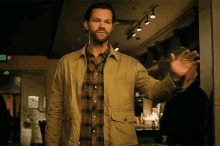 a man in a plaid shirt and a tan jacket waves his hand