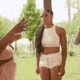 a woman in a white crop top and shorts is standing next to another woman in a pink dress .