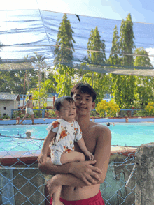 a man holds a baby in front of a pool