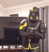 a man in a black and yellow armor standing in front of a flat screen tv