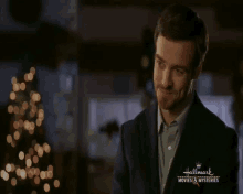a man in a suit and tie is standing in front of a christmas tree .