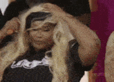 a woman wearing a wig and a black shirt is holding her hair in her hands .