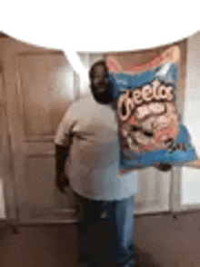 a man is holding a bag of cheetos in his hand .
