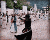 a man in a black robe is standing in front of a crowd of people in traditional clothes