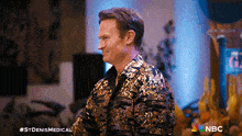 a man in a gold sequined shirt is standing in front of a nbc logo