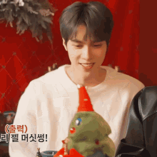 a man in a white shirt is holding a stuffed christmas tree with a red hat on it