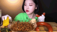 a woman in a green shirt is eating noodles and holding a sausage