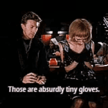 a man and a woman are sitting next to each other and the woman is wearing gloves .