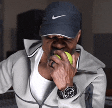 a man wearing a nike hat is biting into a green tennis ball