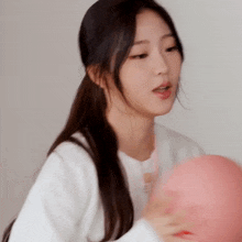 a woman in a white shirt is holding a pink ball in her hands