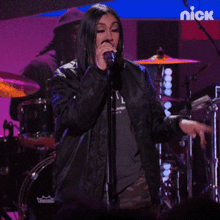 a woman singing into a microphone in front of a nick banner