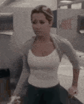 a woman in a white tank top and a grey sweater is standing in a bathroom .