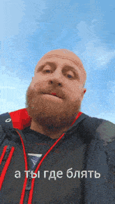 a bald man with a beard is wearing a black and red jacket with a blue sky in the background