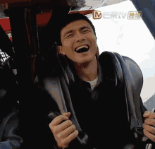 a man is laughing while riding a roller coaster with a chinese tv logo in the background