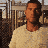 a man wearing a leonida marine center shirt stands in front of a chain link fence