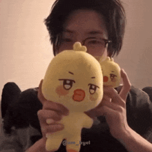 a man wearing glasses is holding a stuffed yellow duck .