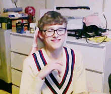 a boy wearing glasses and a striped sweater is smiling in front of a dresser that says sweets for round