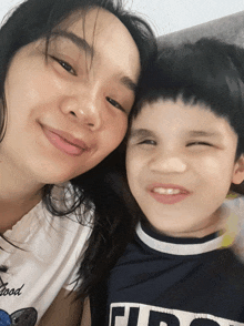 a woman and a boy are posing for a picture and the boy is wearing a shirt that says " good " on it