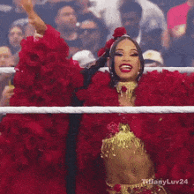 a woman in a red and gold outfit is standing in a ring with her hand in the air .