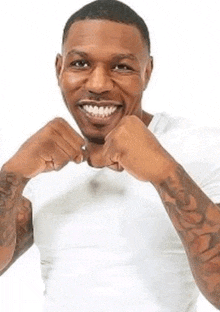 a man with tattoos on his arms is smiling and holding his fists up .