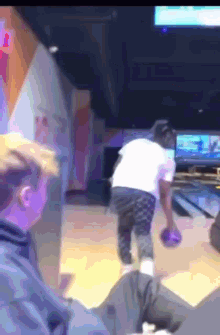 a man is throwing a bowling ball on a bowling alley while another man watches