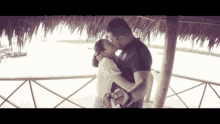a man and woman kissing under a thatched roof overlooking a body of water