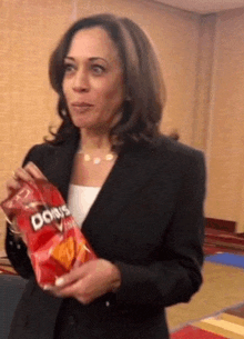 a woman in a suit is holding a bag of doritos .