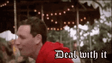 a man in a red hoodie is standing in front of a merry go round with the words deal with it on the bottom