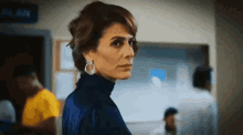 a woman in a blue dress and earrings is standing in a hallway .