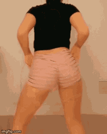 a woman in a black shirt and pink shorts is dancing in a room .