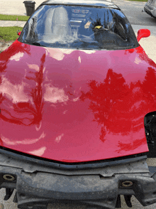 a red sports car with the hood removed is parked on a street