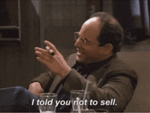 a man with glasses and a cigar says " i told you not to sell " while sitting at a table