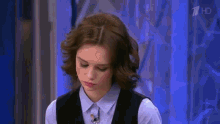 a woman in a blue shirt and black vest on a tv show