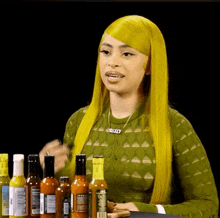 a woman with yellow hair is standing in front of a table full of hot sauce bottles .