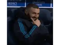 a man is sitting in a chair with his hand on his chin in front of a sign that says champions league