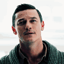 a man wearing a green sweater and a tan shirt looks at the camera