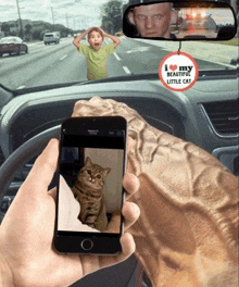 a person taking a picture of a cat in a car with a i love my beautiful little cat hanging from the rear view mirror