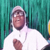 a man wearing a hat and glasses is standing in front of a green background .