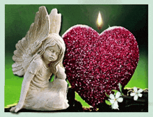 a statue of an angel sits next to a red heart with a lit candle