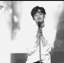 a black and white photo of a man singing into a microphone on a stage .