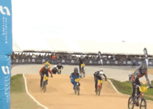 a group of people are riding bicycles on a track with a blue sign that says ' s ' on it